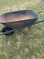 Side angle showing metal body with rust, wheel and handles resting on grass