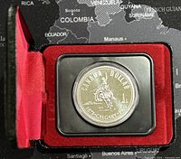 Silver dollar coin inside red velvet display case on world map background.