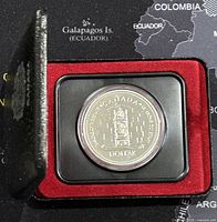 Closed shot of the silver dollar coin in its display case with red velvet interior.