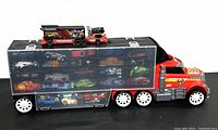 Side view of red and silver Hot Wheels semi-truck case loaded with multiple Hot Wheels cars visible through compartments.