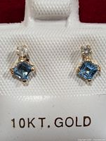 Front view of both earrings showing the blue square-cut topaz and round diamond stones set in 10KT gold.