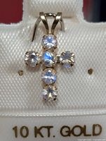 Close-up of cross-shaped pendant with six moonstones set in 10KT gold on a white display card marked '10 KT. GOLD'