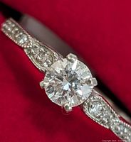 Close-up front view on red background showing central round-cut lab diamond and side accents.