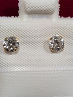 Pair of 14KT gold earrings with round clear cubic zirconia stones in a white jewelry card