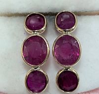 Front view of pair of 10KT gold earrings each set with three oval faceted natural glass-filled rubies in bezel settings.