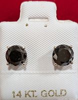Close-up image of two round black diamond stud earrings set in 14KT gold on a display card.