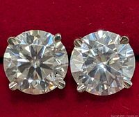 Close-up photo showing the front of the two round brilliant cut moissanite stones mounted in 14KT gold four-prong settings on a red surface.