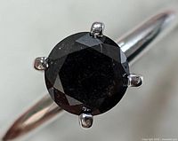 Close-up image showing round black diamond in four-prong 14KT white gold setting with polished band.