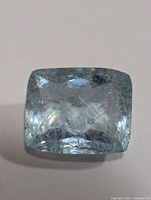 Top view of the loose aquamarine gemstone showing cushion cut and pale blue color with inclusions.