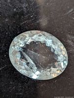 Oval cut genuine aquamarine light blue gemstone with faceted checkerboard surface. Shows internal inclusions and natural markings.