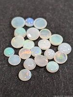 Multiple genuine Australian opal cabochons placed on black background showing their iridescence and various sizes