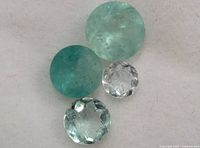 Four faceted gemstones placed on a white surface, two green Colombian emeralds and two clear stones.