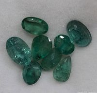 Close-up of eight genuine emerald gemstones showing various shapes and natural inclusions.