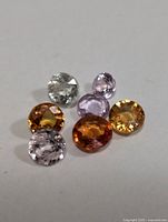 Seven loose faceted sapphires of varying colors on white background.