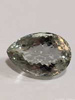 Close-up view of pear-shaped green amethyst gemstone showing faceted surface and transparency