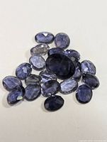 Top view of multiple oval faceted iolite gemstones arranged on a white background, highlighting their color and cut.