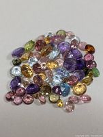 Multiple assorted multi-color genuine faceted gemstones in various shapes and sizes laid out on a white background.