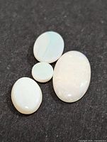 Four genuine opal cabochon stones placed on a dark surface, showing white base color with iridescence and varying sizes and shapes.