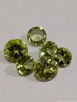 Top view of seven round faceted peridot gemstones arranged together on a white background, showing vivid green color and brilliance.