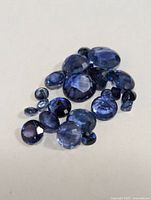 Close-up photo showing multiple loose faceted blue sapphires in various shapes and sizes on a plain surface.