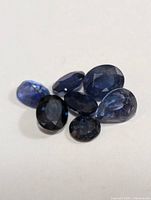 Seven loose sapphires on a white background showing various cuts and blue hues.