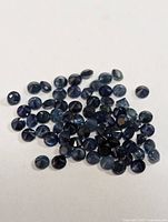 Photo of approximately 54 loose round cut blue sapphires arranged on a white background, showing the facets and deep blue color of the stones.