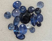 Collection of blue sapphires, loose and faceted, various shapes and sizes resting on white background.