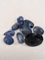Close-up photos of nine genuine sapphire gemstones in various blue hues and sizes, shown on a white background.