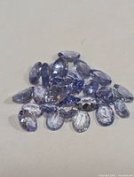 Pile of multiple oval faceted tanzanite gemstones showing various angles and color hues from blue to violet.