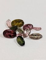 Photo showing multiple small faceted tourmaline gemstones of various colors and shapes on a white background.