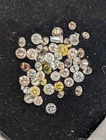 Top-down close-up image of multiple small round diamonds in white, yellow, and light brown colors on a black felt background.