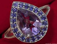 Close-up image of pear-shaped faceted amethyst ring with halo of small round cubic zirconia stones, set in sterling silver with a polished band.