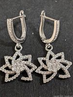 Pair of silver dangle earrings showing floral design with cubic zirconia stones and hinged lever back clasps.