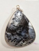 Front and angled view of the silver pendant featuring a pear-shaped dendritic agate gemstone with black fern-like inclusions on a white and translucent base.