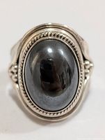 Front view of silver ring with large oval hematite cabochon gemstone, showing polished surface and twisted wire silver detailing.