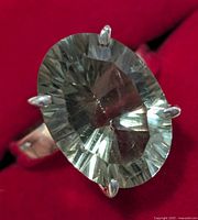 Close-up photo showing large oval green amethyst gemstone set in silver ring against red background