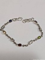 Full view of silver bracelet showing alternating oval gemstones and elephant-shaped links on white background
