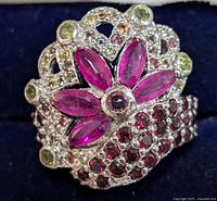 Close-up front view of ornate silver ring with pink marquise-shaped stones and multicolored smaller stones set in intricate floral and swirl pattern on the band.