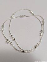 Full view of silver bead-accented delicate chain necklace arranged in a circle to show length and bead pattern.