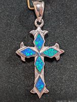 Front view of the silver cross pendant with four blue-green opalite stones set in the arms and base of the cross on a black background.