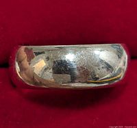 Close-up photo of wider silver band ring showing curved polished surface, some surface scratches and wear.