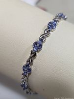 Close-up showing bracelet design with clusters of tanzanite stones and twisted sterling silver links, displayed on a white padded surface.