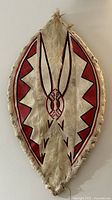 Front view of African tribal warrior shield showing painted symmetrical crescents and triangular motifs on animal hide with fur edges.