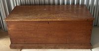 Front view of antique pine blanket box showing rectangular shape, dovetailed joinery, locked keyhole, flat lid surface with visible scratches and patina.