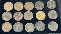 Overview photo of all 15 British Large Penny coins displayed showing front sides with seated Britannia and dates varying from 1860 to 1961. Coins are silver-gray with wear and patina.
