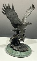 Side angled view of bronze eagle sculpture with wings spread and fish gripped in talons, mounted on green marble base.