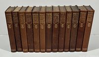 Front view of all 13 book spines showing titles, uniform brown textured hardcover binding with gold embossed lettering and logos.