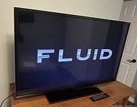 Front view of the Fluid 42-inch LED television on its glass base stand with remote placed in front.