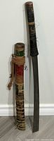 Full view of the sword and its hand painted wooden sheath showing the multi-colored decorations and cord wrapping with tassels.