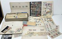 Wide view showing multiple album pages and envelopes containing thousands of stamps in varied conditions and styles.